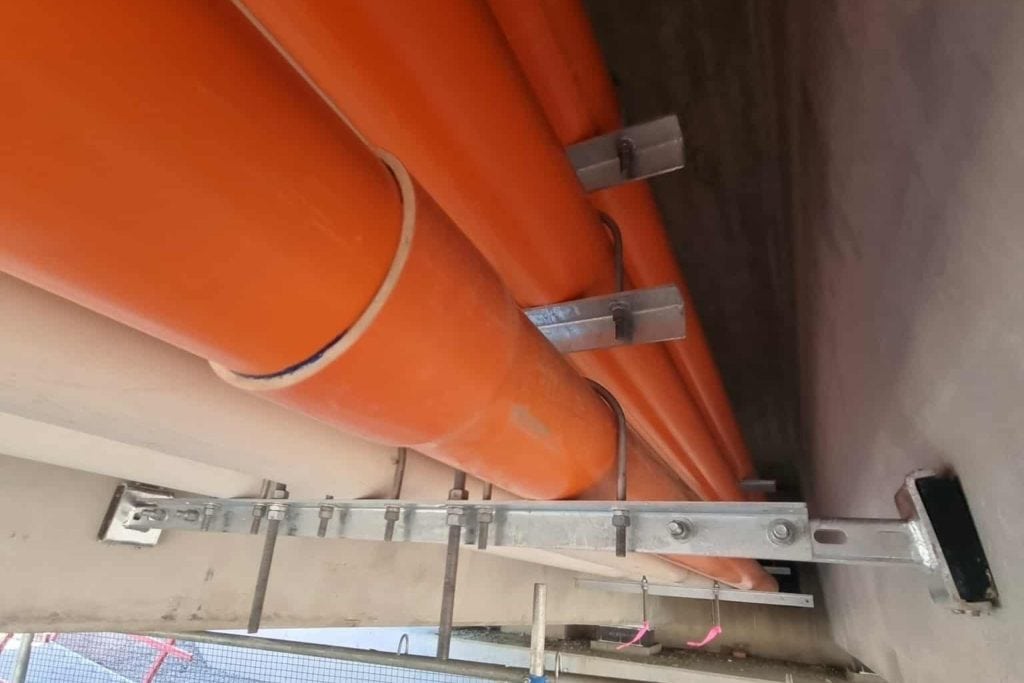 Custom electrical conduit supports for Tram Grade Separation Project Close-up of Apex Energy Australia custom conduit support brackets and orange electrical conduits installed beneath an Adelaide tram overpass for the Tram Grade Separation Project.