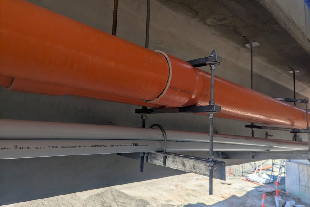 Custom conduit suspension brackets for Tram Grade Separation Project Close-up of Apex Energy Australia custom suspension brackets supporting electrical and communications conduits beneath a tram overpass for the Tram Grade Separation Project.